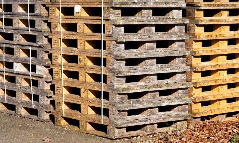 A large group of timber block pallets stacked up together in a square formation outside of a building.