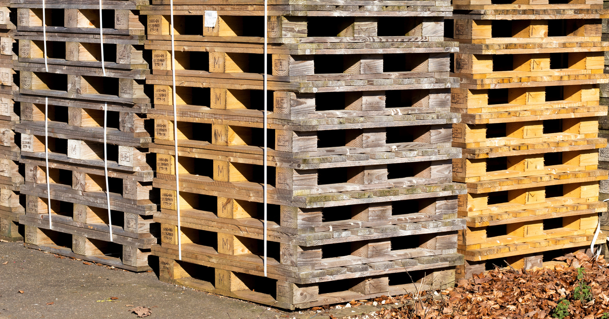 A large group of timber block pallets stacked up together in a square formation outside of a building.