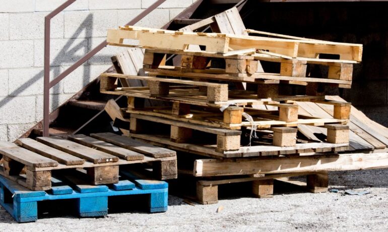 Two stacks of broken wood pallets sit beside a stairway on an industrial site. The wood pallets have broken and frayed edges.