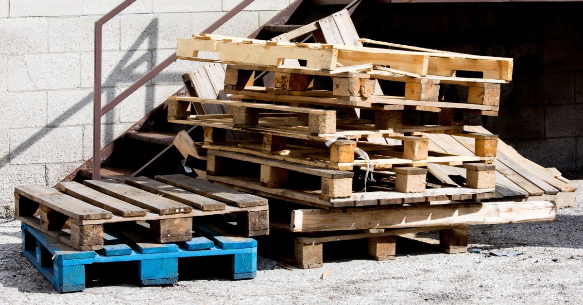 Two stacks of broken wood pallets sit beside a stairway on an industrial site. The wood pallets have broken and frayed edges.