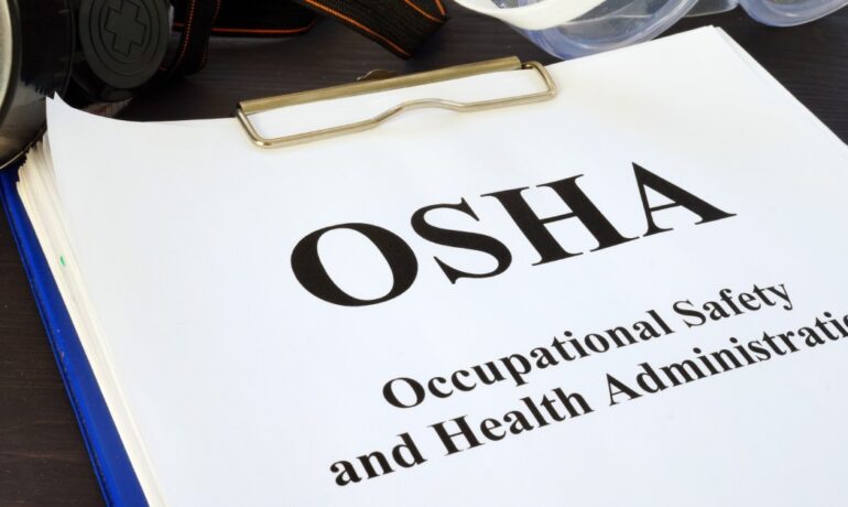 A blue clipboard holds a pile of papers. The top sheet says "OSHA - Occupational Safety and Health Administration."