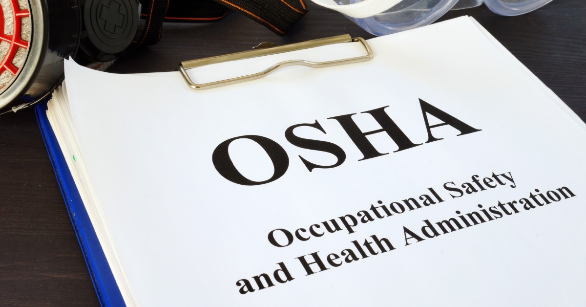 A blue clipboard holds a pile of papers. The top sheet says "OSHA - Occupational Safety and Health Administration."