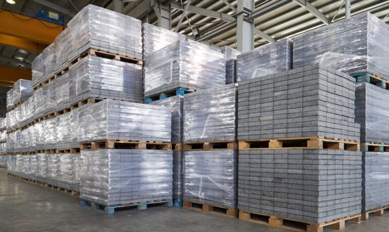 A large warehouse with paving slabs on wood pallets stacked up to four pallets high and wrapped in plastic.