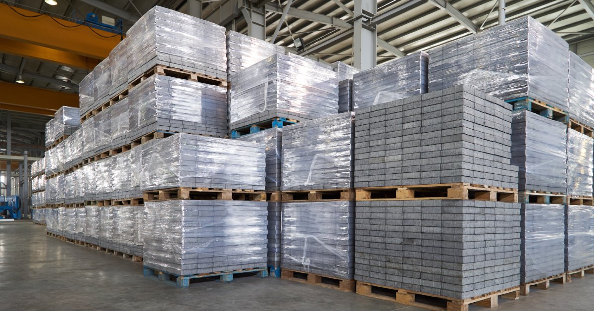 A large warehouse with paving slabs on wood pallets stacked up to four pallets high and wrapped in plastic.