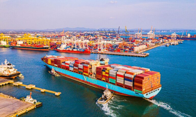 A large cargo ship filled with containers enters a busy port, ready for unloading and international shipping.