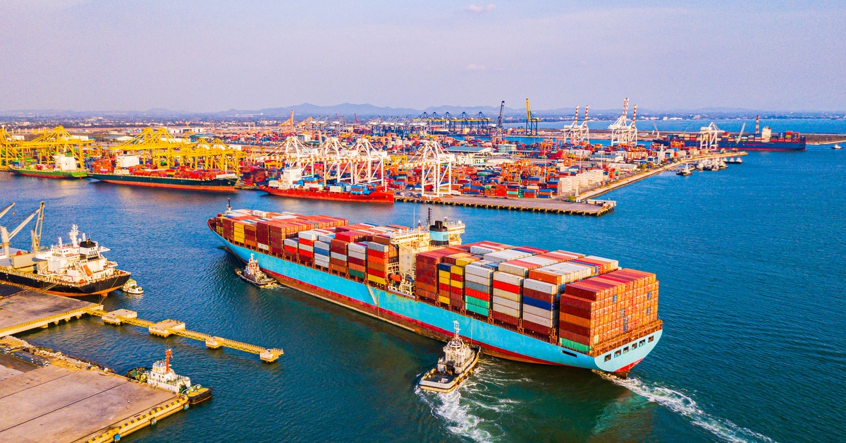 A large cargo ship filled with containers enters a busy port, ready for unloading and international shipping.